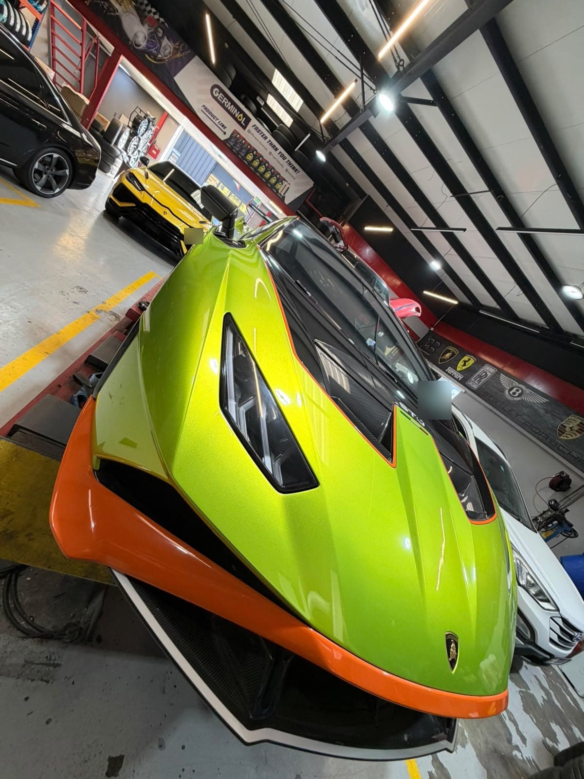 Front of a Lamborghini Huracán STO on the alignment lift in the Juventus Tyres workshop, Dubai, below the wall of marque badges