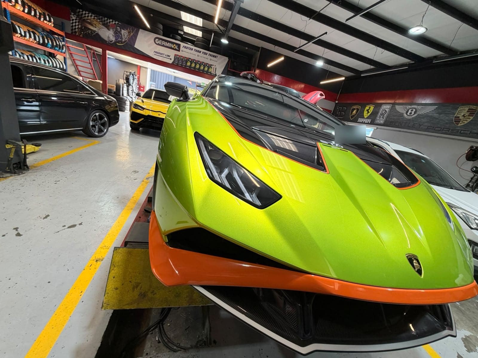 Lime green and orange Lamborghini Huracán STO on the alignment lift at Juventus Tyres in Al Quoz, Dubai, with a yellow Urus behind it