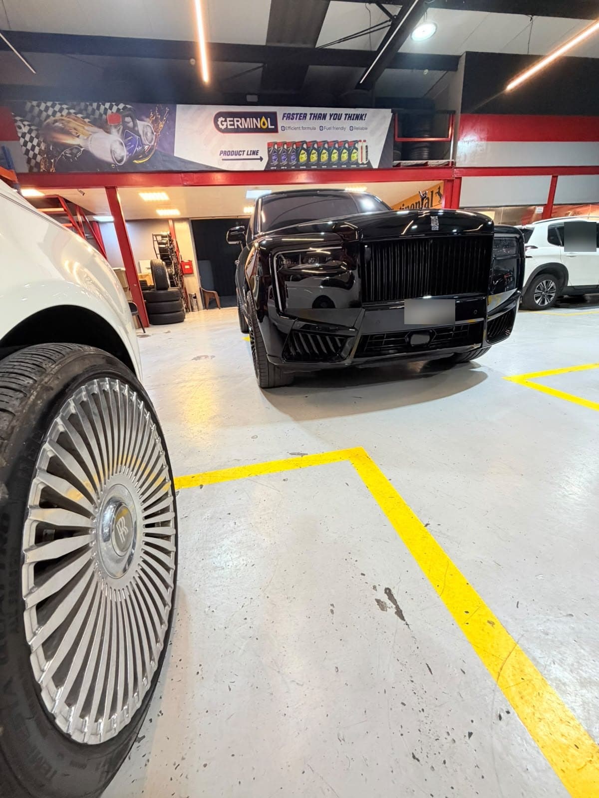 Black Rolls-Royce Cullinan in the Juventus Tyres workshop, Dubai, beside the polished multi-spoke wheel of another Rolls-Royce