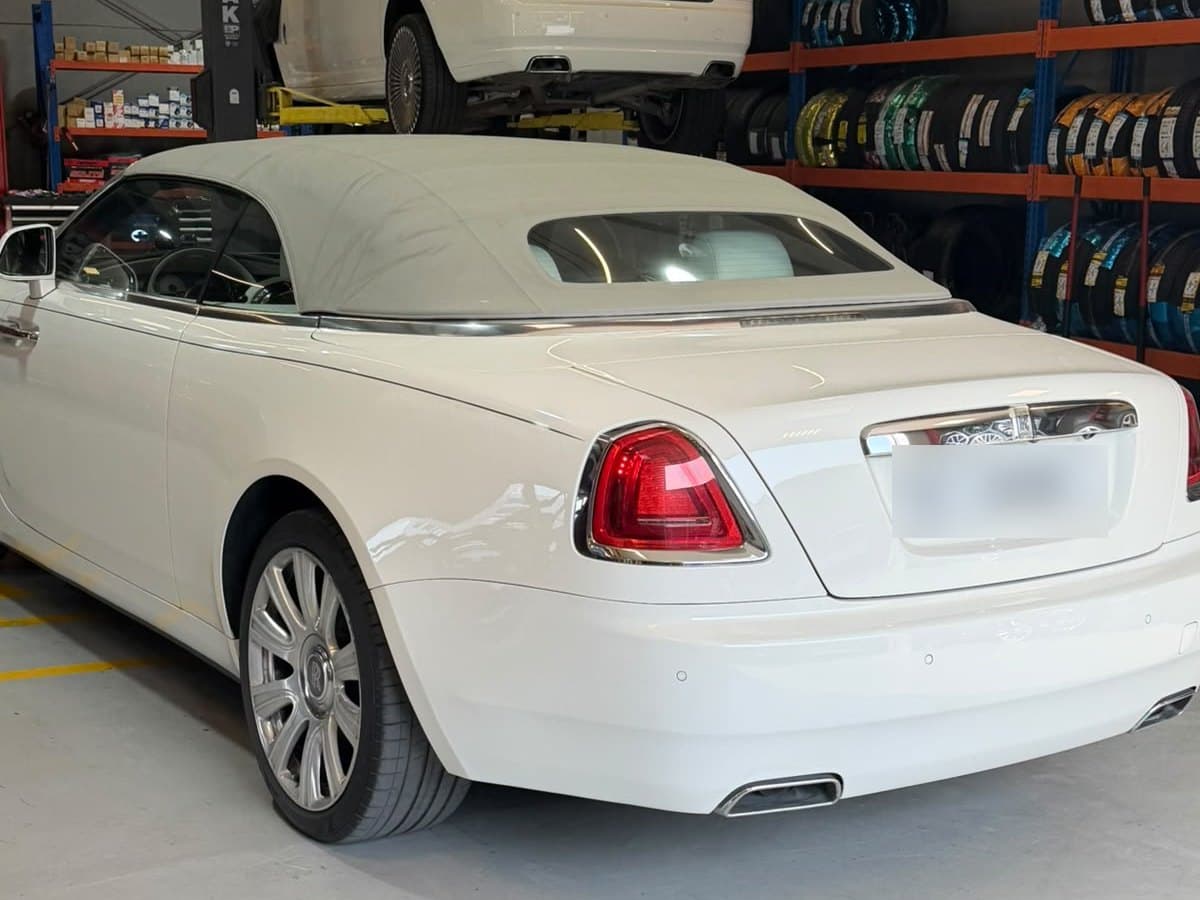 White Rolls-Royce Dawn with its soft top up in the Juventus Tyres workshop in Al Quoz, Dubai, with another white car raised on the two-post lift behind it and racks of new tyres